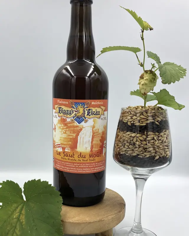 Bouteille de Saut du Moût à côté d'un verre de malt et de houblon